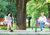 A conversation. In a park. Between two women. Sitting on benches.